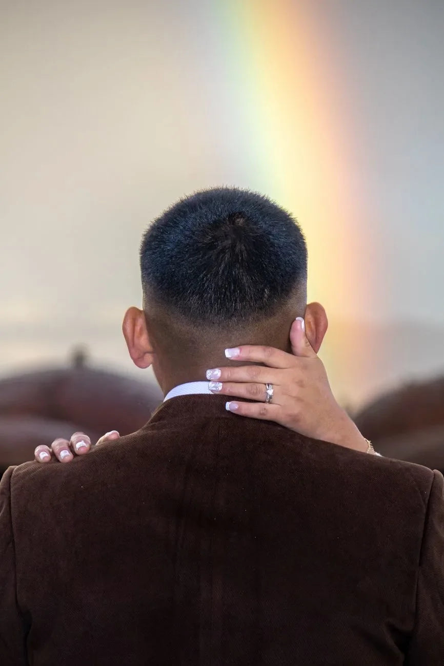 Un couple partage un moment intime avec un arc-en-ciel en arrière-plan, symbolisant l'amour et l'unité.