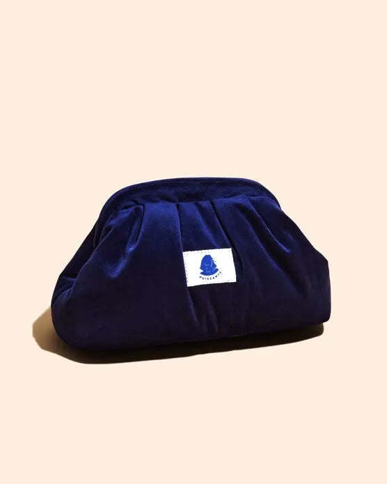 sac de toilette en velours bleu marine avec un logo sur une étiquette blanche sur le devant sur fond beige