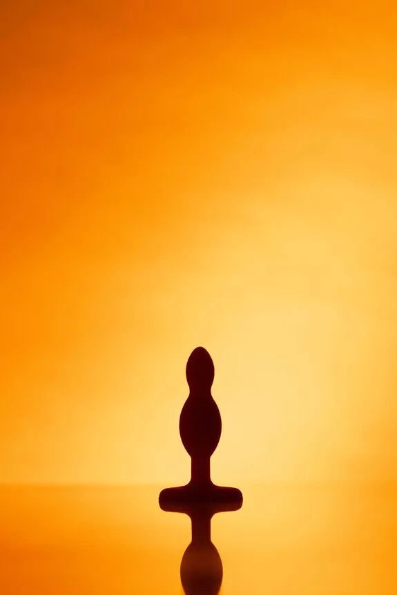 Jouet intime en silicone silhouette noire sur fond orange saisissant.