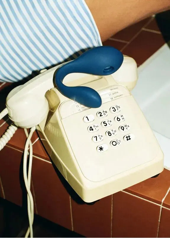Vibromasseur bleu ergonomique sur téléphone vintage, design moderne et discret pour plaisir intime.