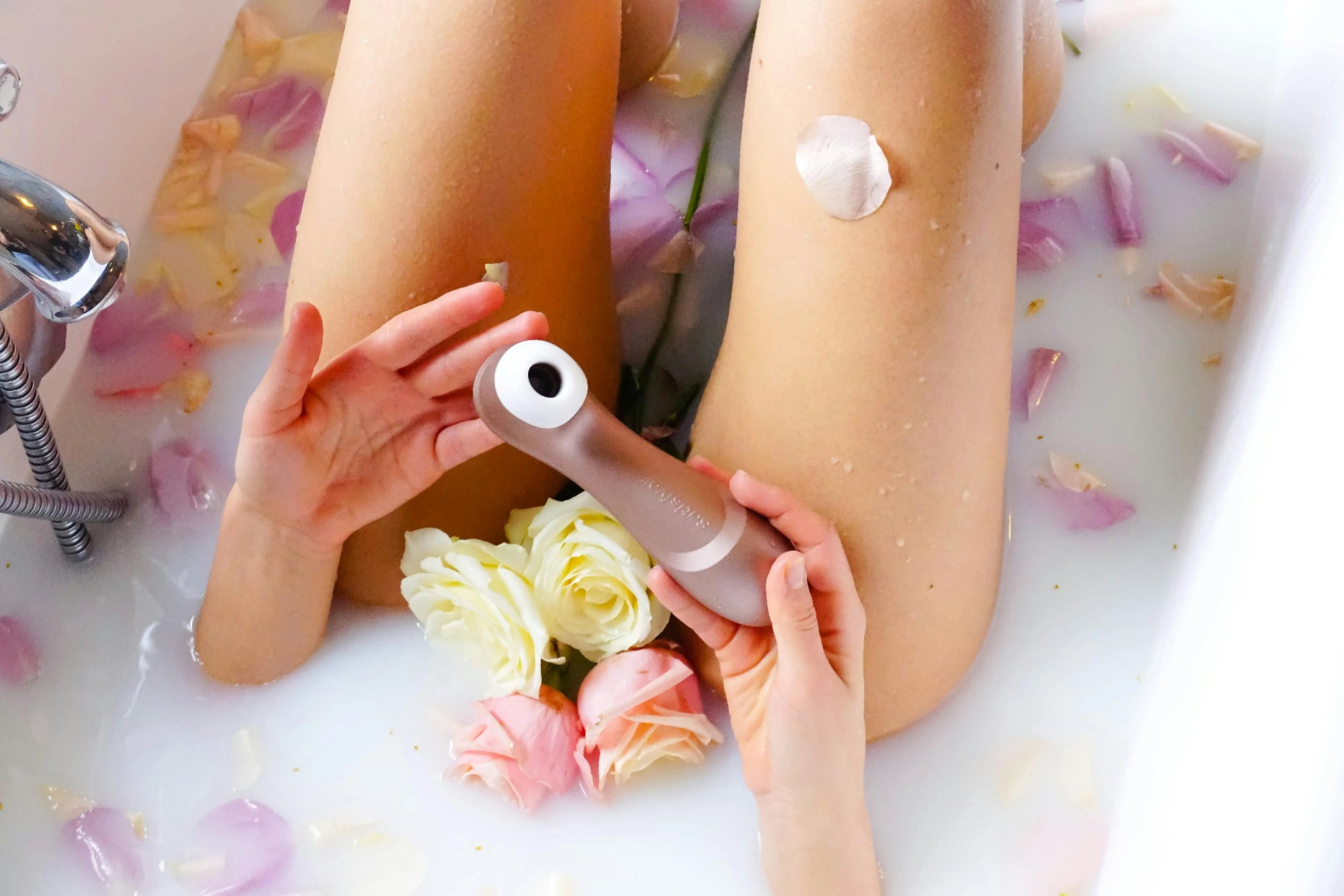 Une femme se détend dans une baignoire remplie de fleurs, avec un vibromasseur à ses côtés.